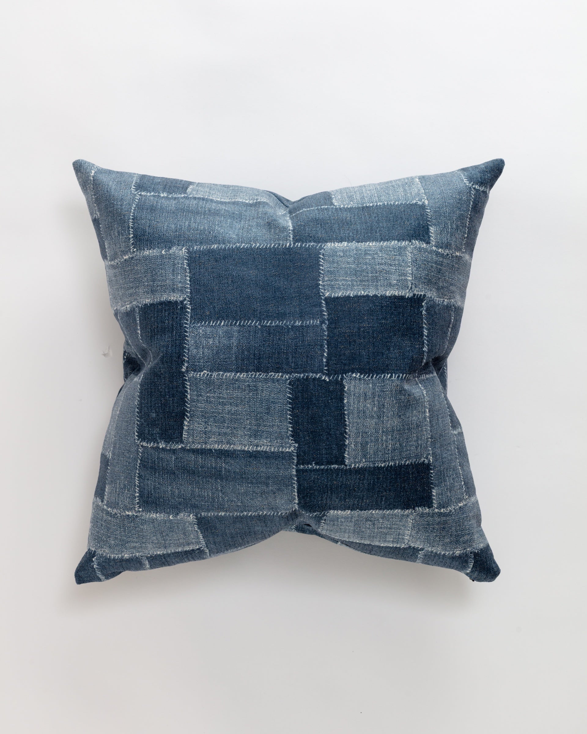 The Norwalk Maggie Pillow is a square throw pillow with a blue denim patchwork design and trimmed edges, offering a textured and cozy feel on a white background, complete with a plush down insert.