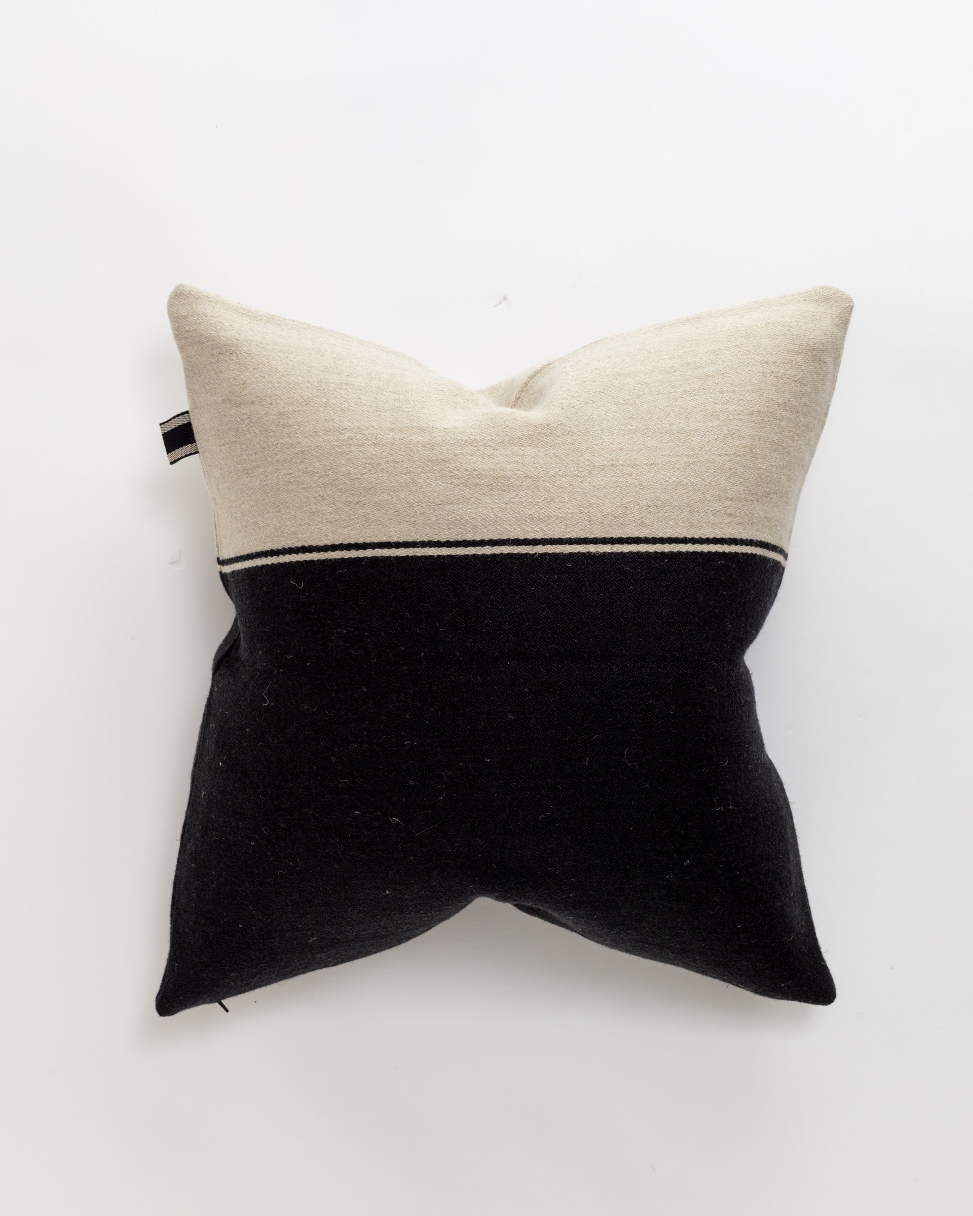 The Marshall Pillow by Libeco Home is a square throw pillow with a classic two-tone design in cream and black, separated by a thin line. Made of luxurious linen and wool, it is elegantly displayed against a plain white background.