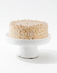 A decorated vanilla cake sits on the Montes Doggett 4807-L Cake Stand no. 807 L. The round cake features intricate, creamy swirls and textured patterns on its sides and top, giving it an elegant appearance. Handmade by skilled artisans, the stand enhances the cake against a plain white background.