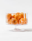 A clear, handcrafted Scalloped Glass Bowl by Zodax filled with several orange tangerines, set against a white background. This elegant decor piece adds a touch of sophistication to any setting.