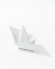 The 5419 Sail Boat no. 419 by Montes Doggett is a high-fired ceramic sculpture resembling an origami paper boat, set against a plain white background. Handmade in Peru, this piece captures the intricate folds and creases of a traditional paper boat, offering a minimalist and delicate aesthetic.