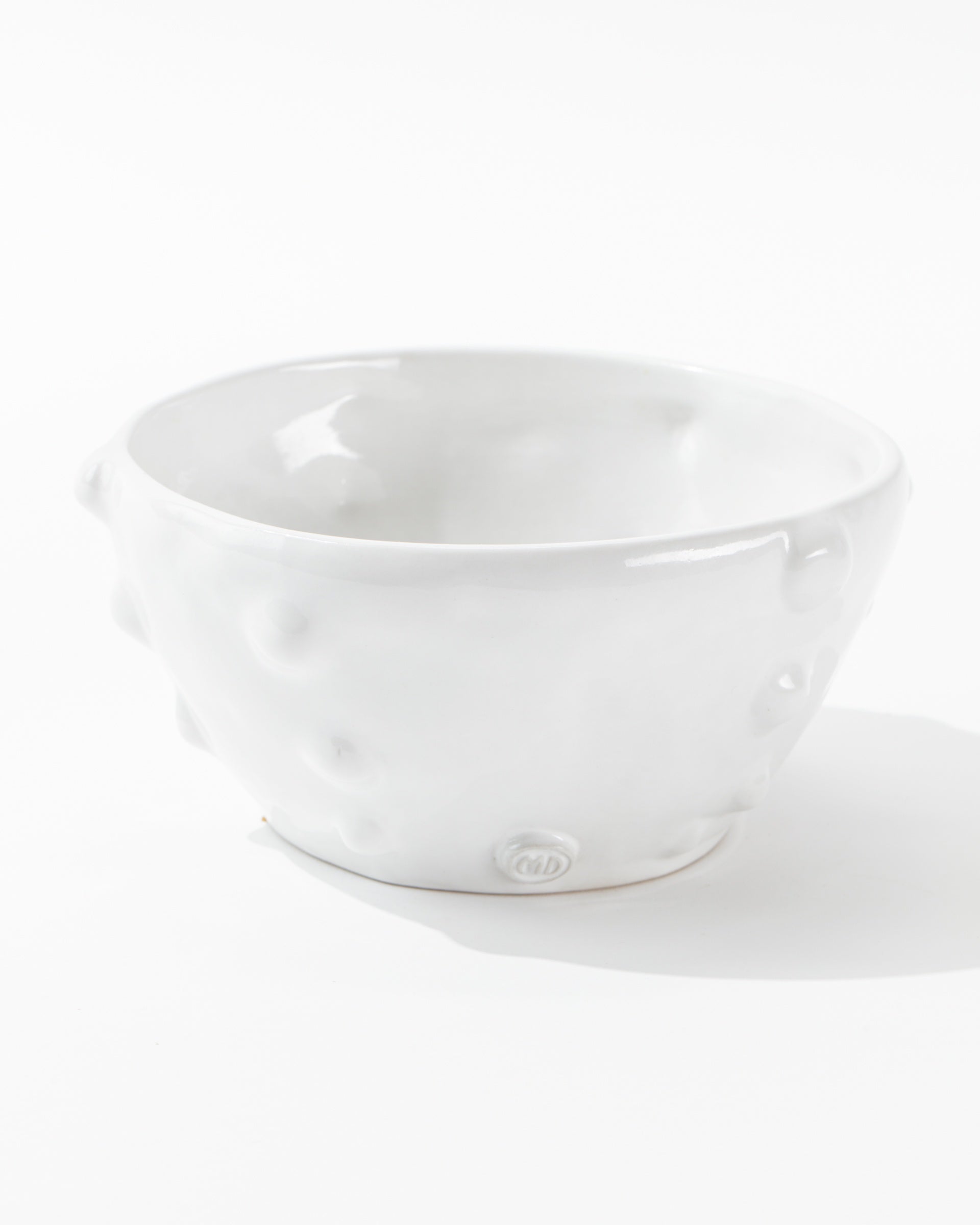 Bowl No. 130 from Montes Doggett, a handmade ceramic piece with a textured surface marked by dimple-like indentations, is centrally placed against a plain white background. Crafted using traditional techniques, this bowl boasts a glossy finish and embodies a minimalist, modern design.