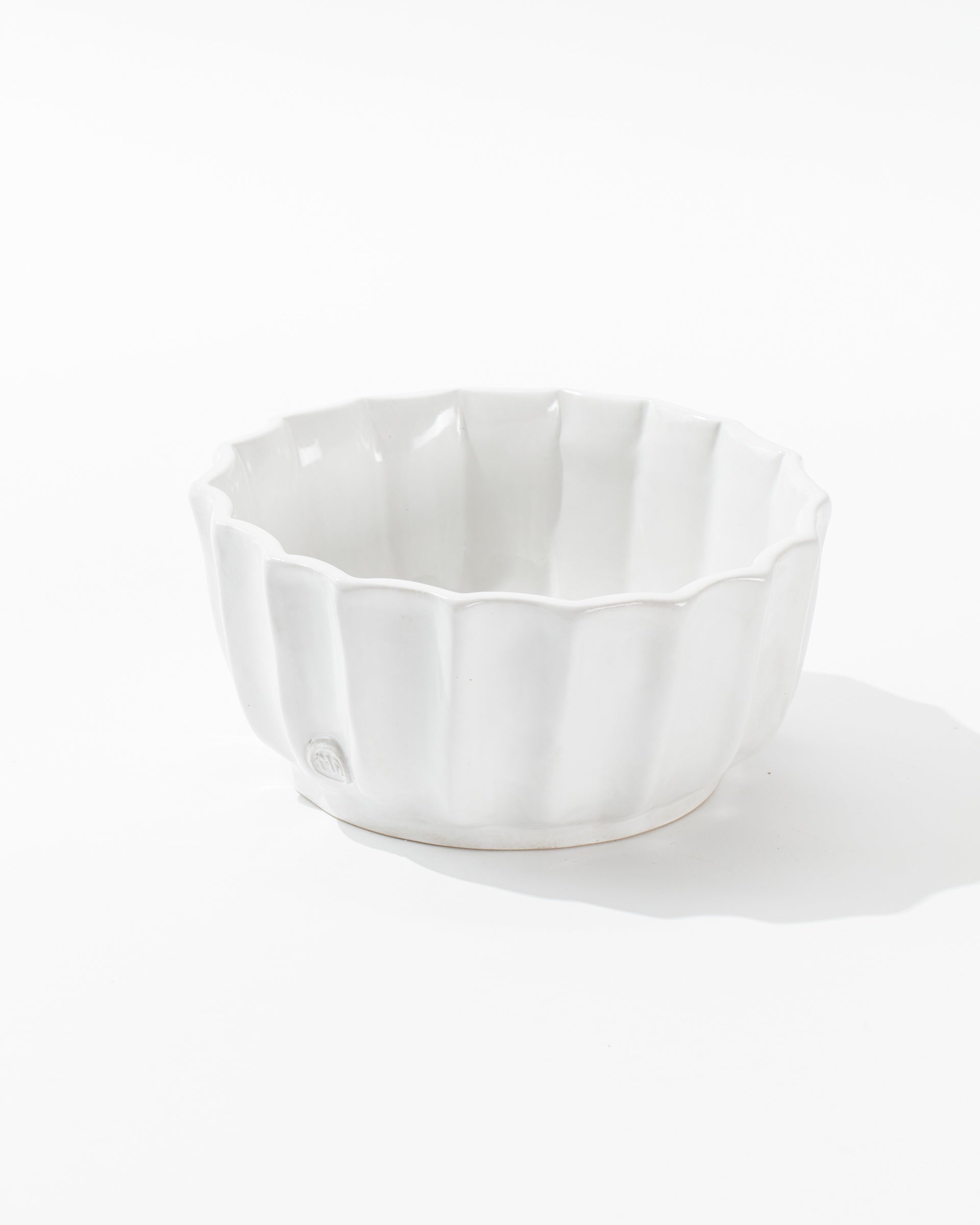 The Montes Doggett 5131 bowl no. 131 is a white ceramic piece featuring a scalloped edge and a glossy finish. This handcrafted bowl, with its shallow design that displays artisanal excellence, has a maker's stamp at the base and is photographed against a plain white background.