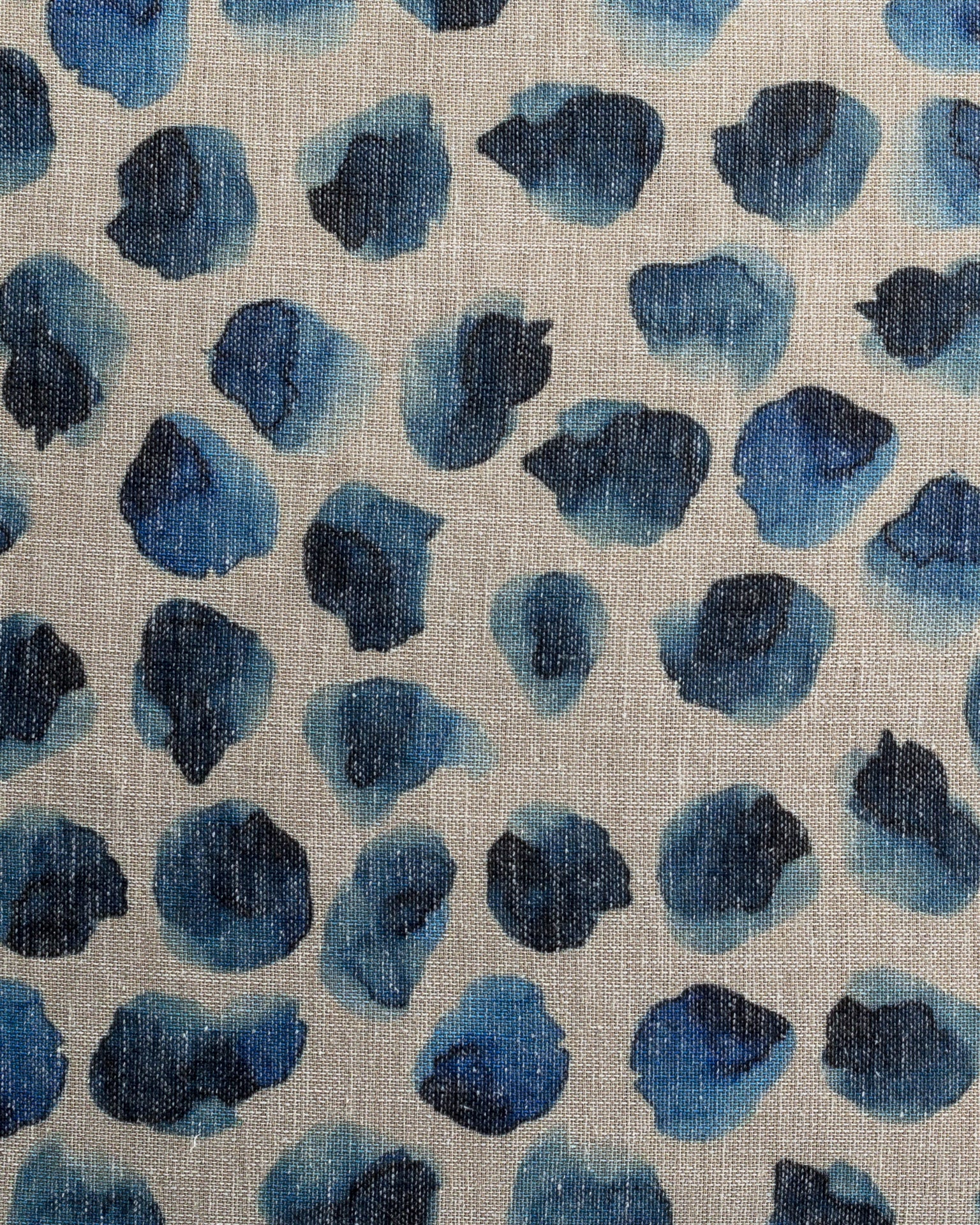 Close-up of a Gabby Blurry Dot Indigo Pillow 26x26 featuring abstract blue and black splotches on a textured beige bungalow background, resembling a watercolor design.