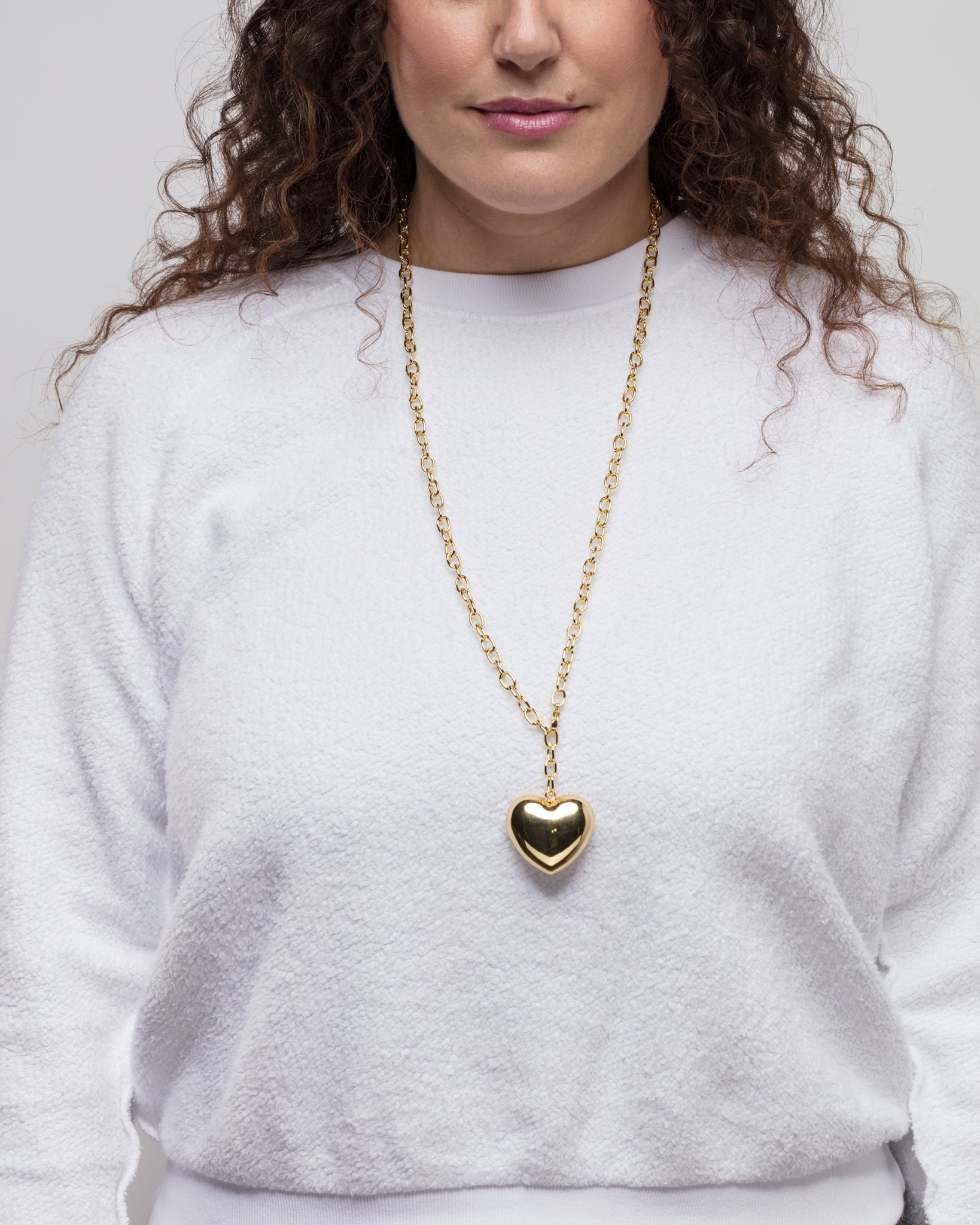 A person with curly hair is wearing a white, long-sleeved top and a long gold necklace featuring a large heart-shaped pendant on a 33&quot; chain. The background is plain white.

Revised:
A person with curly hair is wearing a white, long-sleeved top and a Lucky Star Bubble Heart Necklace. The background is plain white.