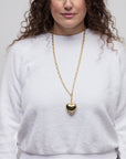 A person with curly hair is wearing a white, long-sleeved top and a long gold necklace featuring a large heart-shaped pendant on a 33" chain. The background is plain white.

Revised:
A person with curly hair is wearing a white, long-sleeved top and a Lucky Star Bubble Heart Necklace. The background is plain white.