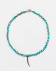 A necklace featuring a sequence of vibrant Designs By Raya turquoise beads with a metallic silver clasp, complemented by a slender, curved pendant resembling a horn or tusk, against a plain white background.