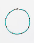 A Designs By Raya turquoise necklace with black and metallic accents, displayed against a white background. The necklace features a simple clasp and embodies Arizona style.