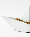 The 5419 Sail Boat no. 419 by Montes Doggett is a white ceramic bowl, handcrafted in Peru and designed to resemble an origami paper boat, elegantly filled with assorted nuts and set against a plain white background. This unique piece of art adds a touch of sophistication to any setting.