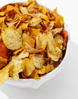 A white handmade Bowl No. 130 by Montes Doggett is filled with a variety of vegetable chips, including sweet potato, beet, and parsnip chips, all against a white background. The chips are golden, orange, and red in color, beautifully showcasing their crispy texture. This durable high-fired piece is crafted using traditional techniques.