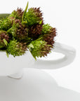 A white Gravy Boat No. 151 from Montes Doggett, filled with small green and brown spiky flowers, is positioned against a white background. The flowers appear fresh and slightly clustered, with the gravy boat slightly angled to highlight its handle and part of its body.