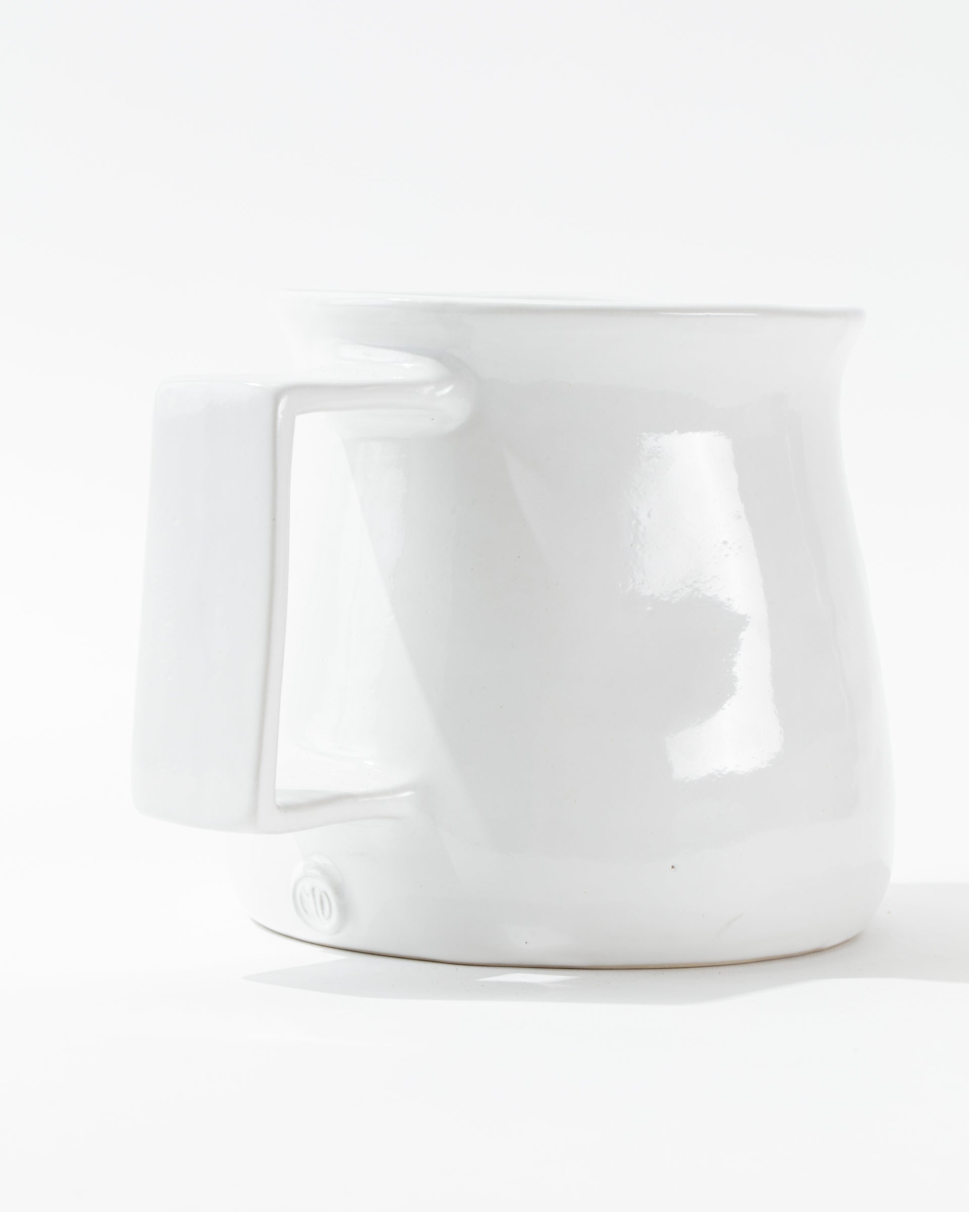 Montes Doggett&#39;s Pitcher No. 750, a glossy white, high-fired ceramic piece, is displayed against a white background. The handmade pitcher has a slightly bulbous shape with a broad handle on its side. Its base features subtle embossed text.