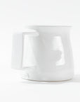 Montes Doggett's Pitcher No. 750, a glossy white, high-fired ceramic piece, is displayed against a white background. The handmade pitcher has a slightly bulbous shape with a broad handle on its side. Its base features subtle embossed text.