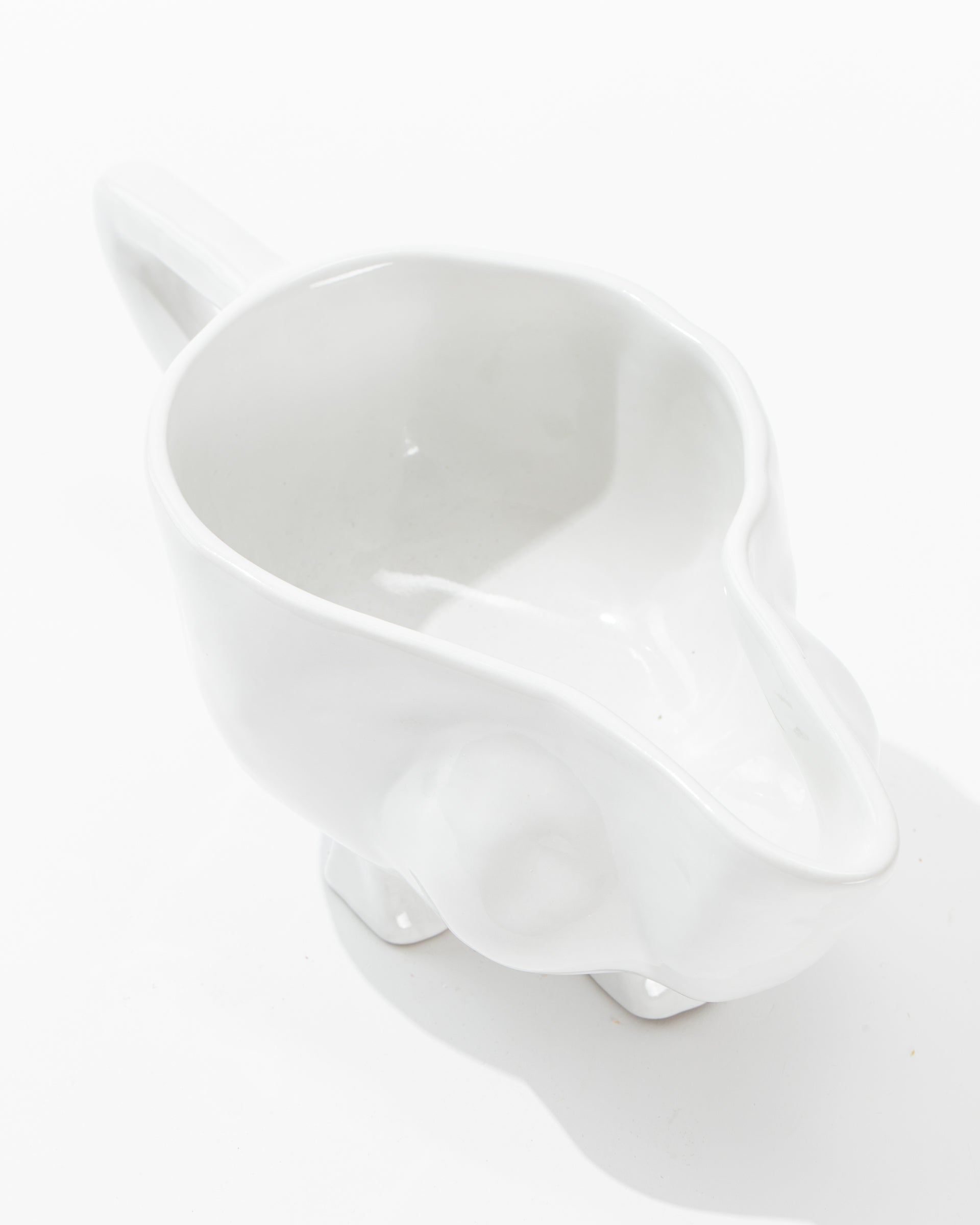 The Gravy Boat No. 151 by Montes Doggett is a white, glossy handmade ceramic piece with a smooth finish and a handle. Crafted from high-fired ceramic, it features a wide spout for easy pouring and stands out beautifully against its plain white background. The design embodies simplicity and modernity, true to the style of Montes Doggett ceramics.