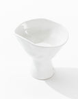 Introducing the 5147 Catchall Bowl No. 147 by Montes Doggett, a sleek and asymmetrical white ceramic piece with a glossy finish. The top features a unique, tilted and irregular rim, while the base is more narrow and cylindrical in shape. Meticulously crafted by skilled artisans, this bowl highlights exceptional durability against its plain white backdrop.