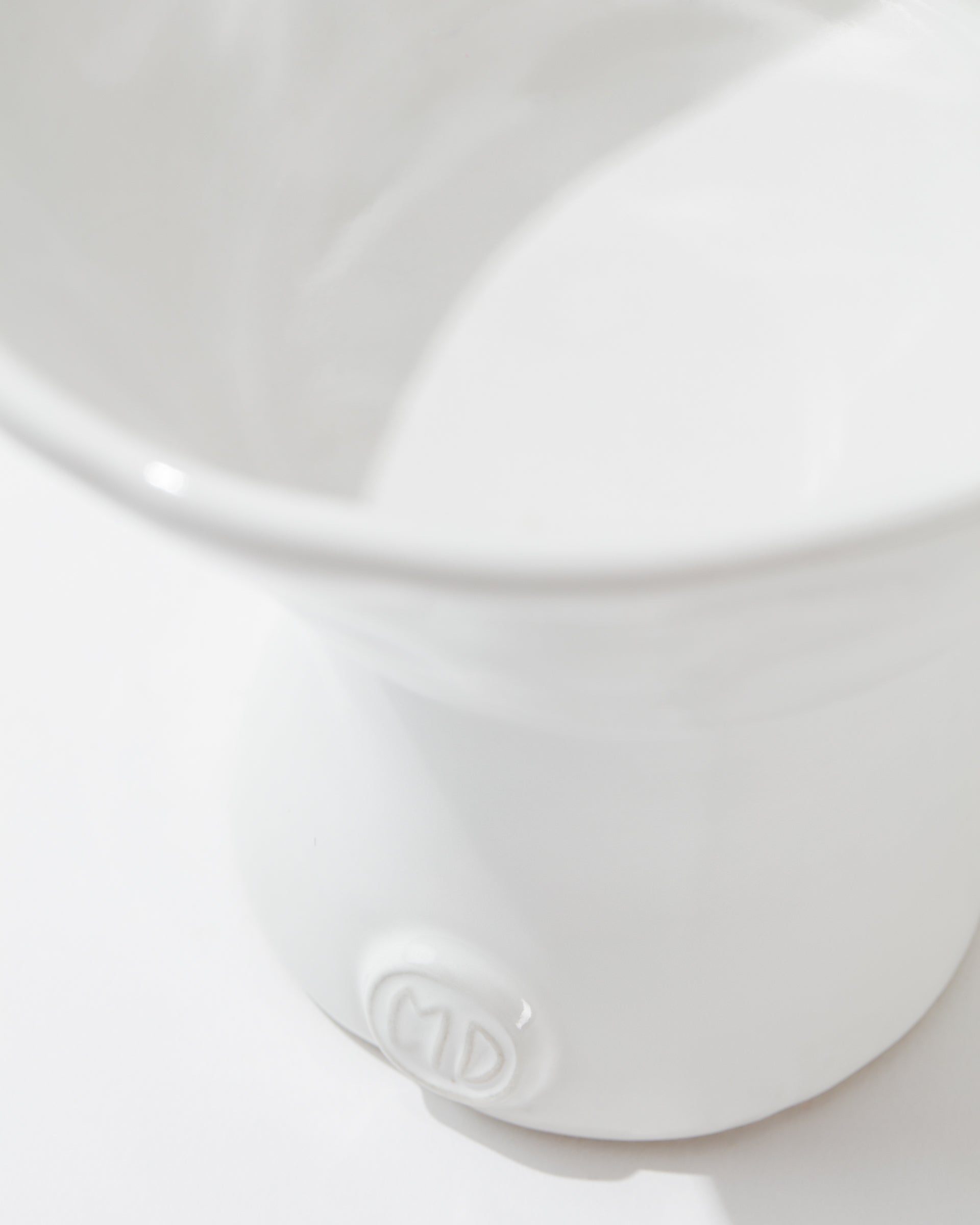 A close-up photo of a white ceramic 5147 catchall bowl no. 147 with a smooth finish. Crafted by skilled artisans at Montes Doggett, the bowl features an embossed logo or monogram near the base displaying the letters &quot;CD.&quot; The focus is on the lower part of the bowl, showcasing its simple yet elegant design and durable craftsmanship.