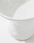 A close-up photo of a white ceramic 5147 catchall bowl no. 147 with a smooth finish. Crafted by skilled artisans at Montes Doggett, the bowl features an embossed logo or monogram near the base displaying the letters "CD." The focus is on the lower part of the bowl, showcasing its simple yet elegant design and durable craftsmanship.