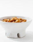 The Catchall Bowl No. 257 by Montes Doggett, crafted using traditional techniques from high fired clay, contains golden-brown fried appetizers, possibly samosas or wontons. Placed against a plain white background, this handmade ceramic dinnerware boasts a unique design with three short legs and a small emblem on the front.