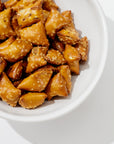 A white Catchall Bowl No. 257 by Montes Doggett, crafted from handmade ceramic dinnerware using traditional techniques, is filled with square-shaped pretzel bites coated in coarse salt. The pretzel bites have a shiny, golden-brown appearance, suggesting they are freshly baked. The bowl is positioned against a light background.