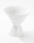 Introducing the Catchall Bowl No. 979 by Montes Doggett – a white, modern ceramic bowl with a unique hourglass shape. The design features a narrow middle section with wide, flaring openings at both the top and bottom. Crafted in Peru, this bowl boasts a glossy finish and is showcased on a plain, white background in the photograph.