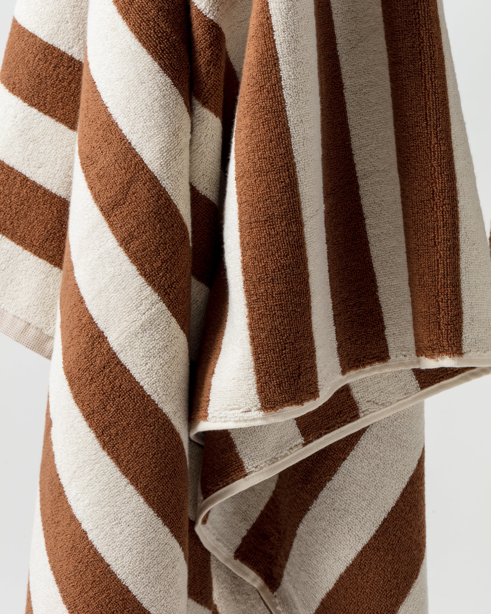 A close-up view of the Maria Pool Towel from Autumn Sonata, featuring bold diagonal stripes in brown and white. The texture appears soft and plush, suggesting a luxurious beach towel. The image showcases the pattern and texture in detail.