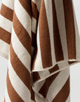 A close-up view of the Maria Pool Towel from Autumn Sonata, featuring bold diagonal stripes in brown and white. The texture appears soft and plush, suggesting a luxurious beach towel. The image showcases the pattern and texture in detail.