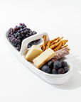 The 4774 Appetizer Platter NO. 774 by Montes Doggett elegantly holds a selection of grapes, two large pieces of cheese, breadsticks, and a piece of cured sausage. The food is artistically arranged against a white background, highlighting the platter's traditional craftsmanship and artisanal charm.