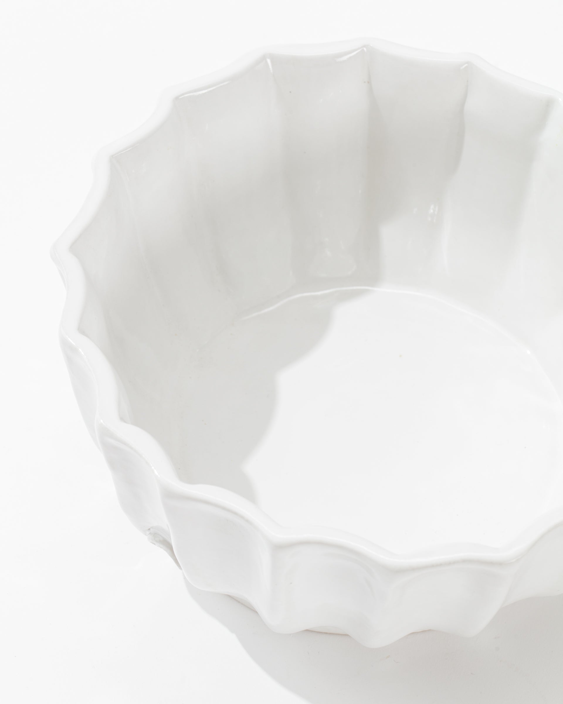 The 5131 bowl no. 131 from Montes Doggett is displayed from a top-down angle, showcasing its handcrafted, high-fired ceramic build with a distinctive scalloped edge. The smooth and glossy inside surface of the bowl reflects light beautifully. The design of this artisanal piece exudes simplistic elegance, standing out against a plain white background.