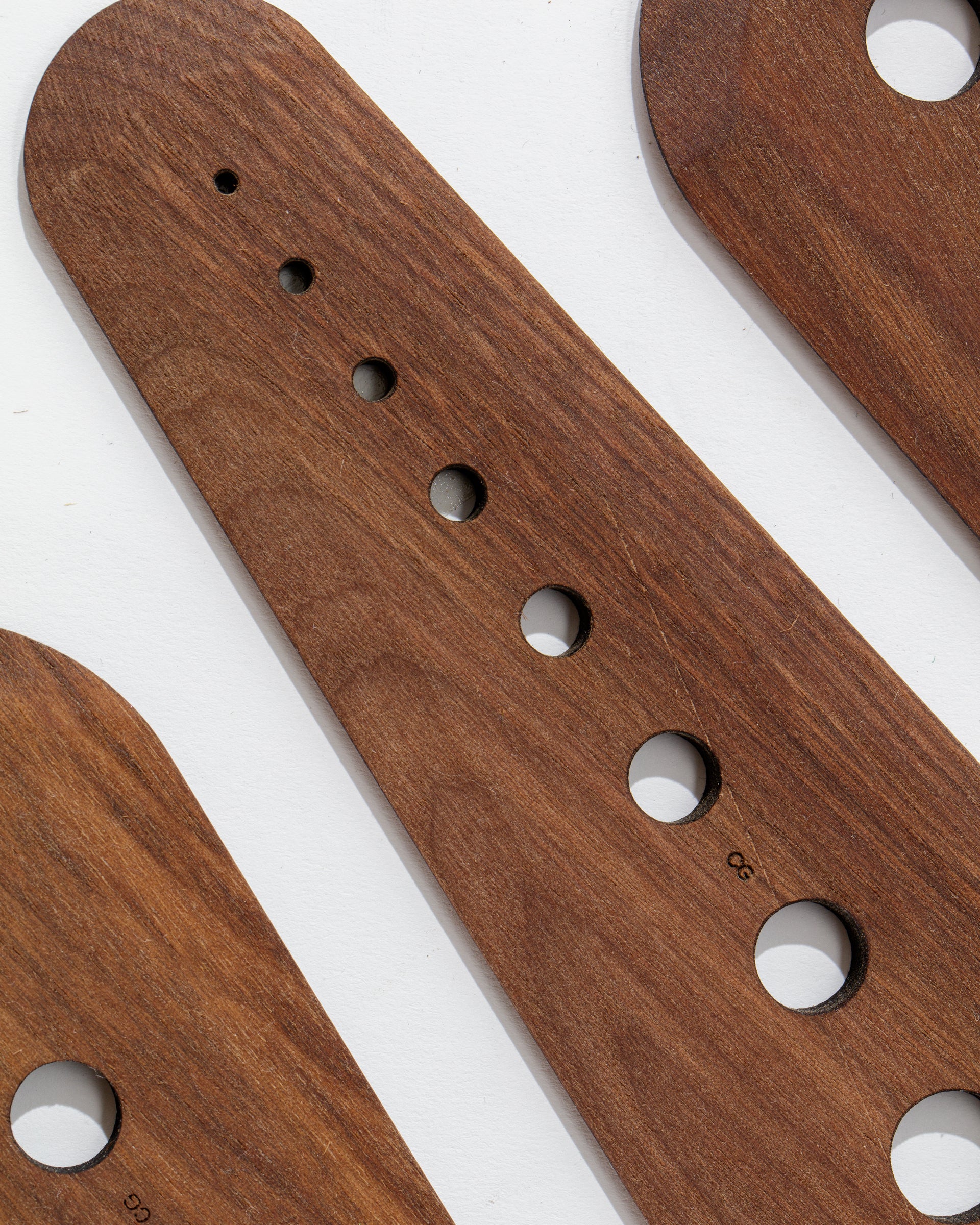 A close-up image of the Faire Herb Stripper showcases its handcrafted wooden design, made from black walnut. It features drilled holes of varying sizes with a smooth, polished finish achieved using food-safe oil. The perfectly circular holes are aligned in a row and have small markings or measurements visible near some of them.