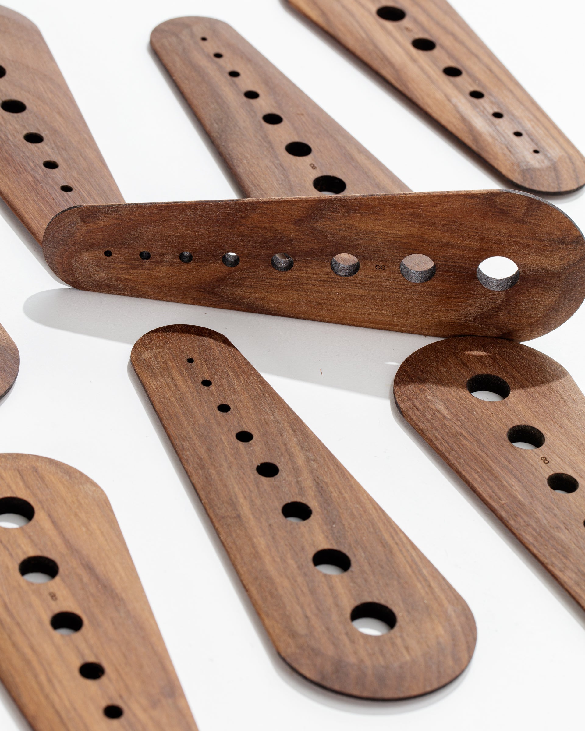 A selection of Faire's Herb Strippers, skillfully handcrafted from black walnut, features an array of cutout holes and diverse shapes, all showcased against a plain white background. These templates differ in length and hole sizes, with some displaying rounded edges. The visible wood grain enhances the texture of each piece. Proudly handmade in St. Louis.