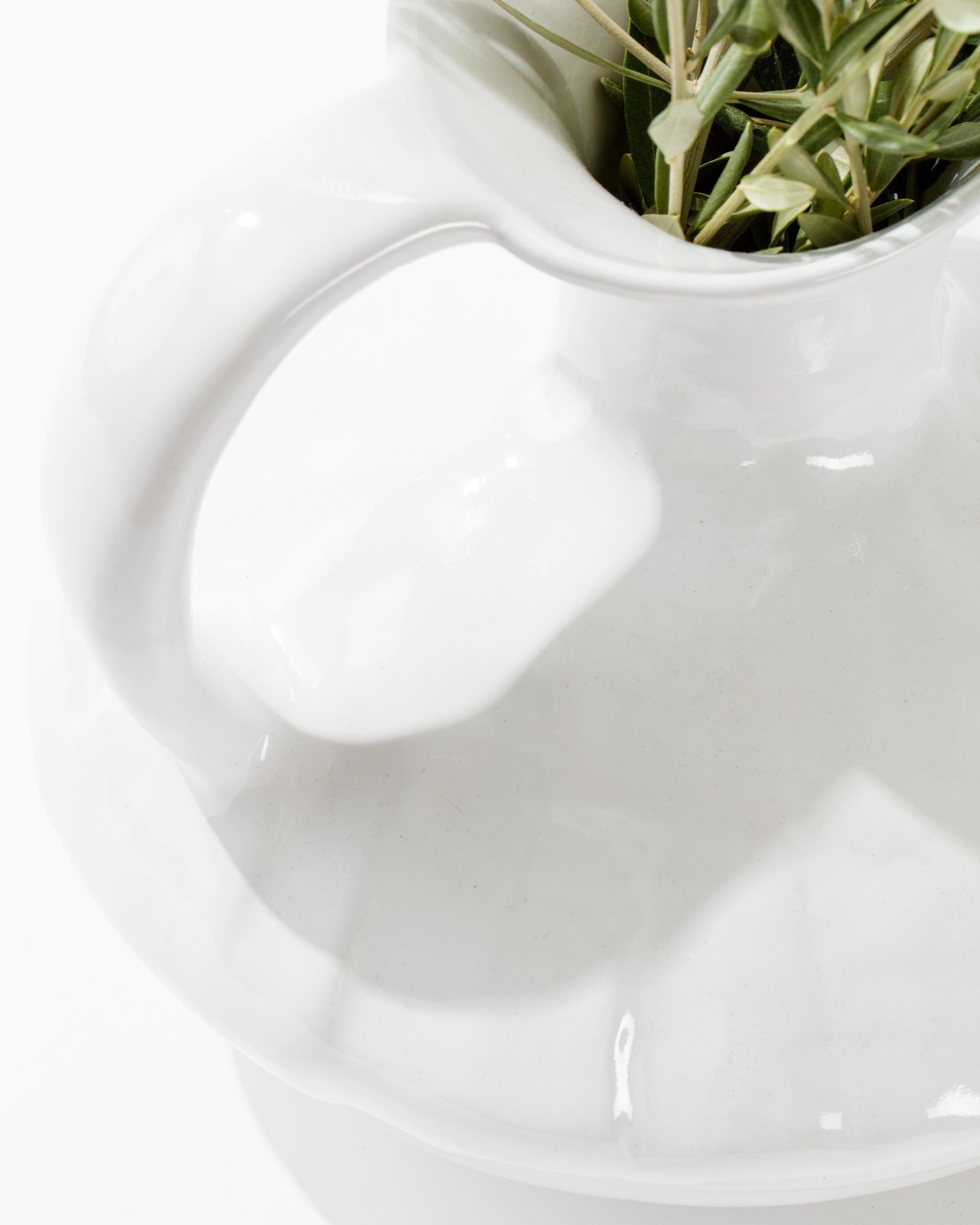 Close-up of the Montes Doggett 5431 Pitcher No. 431, a handmade ceramic jug with a handle, partially filled with a few sprigs of greenery. The image focuses on the smooth, glossy surface of the high-fired pitcher and the delicate leaves, set against a white background.