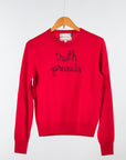 A bright red Cashmere Crewneck by Lingua Franca hangs on a wooden hanger, featuring "truth prevails" embroidered in black script across the chest. Ethically crafted against a plain white backdrop, this stylish piece is as mindful as it is chic.