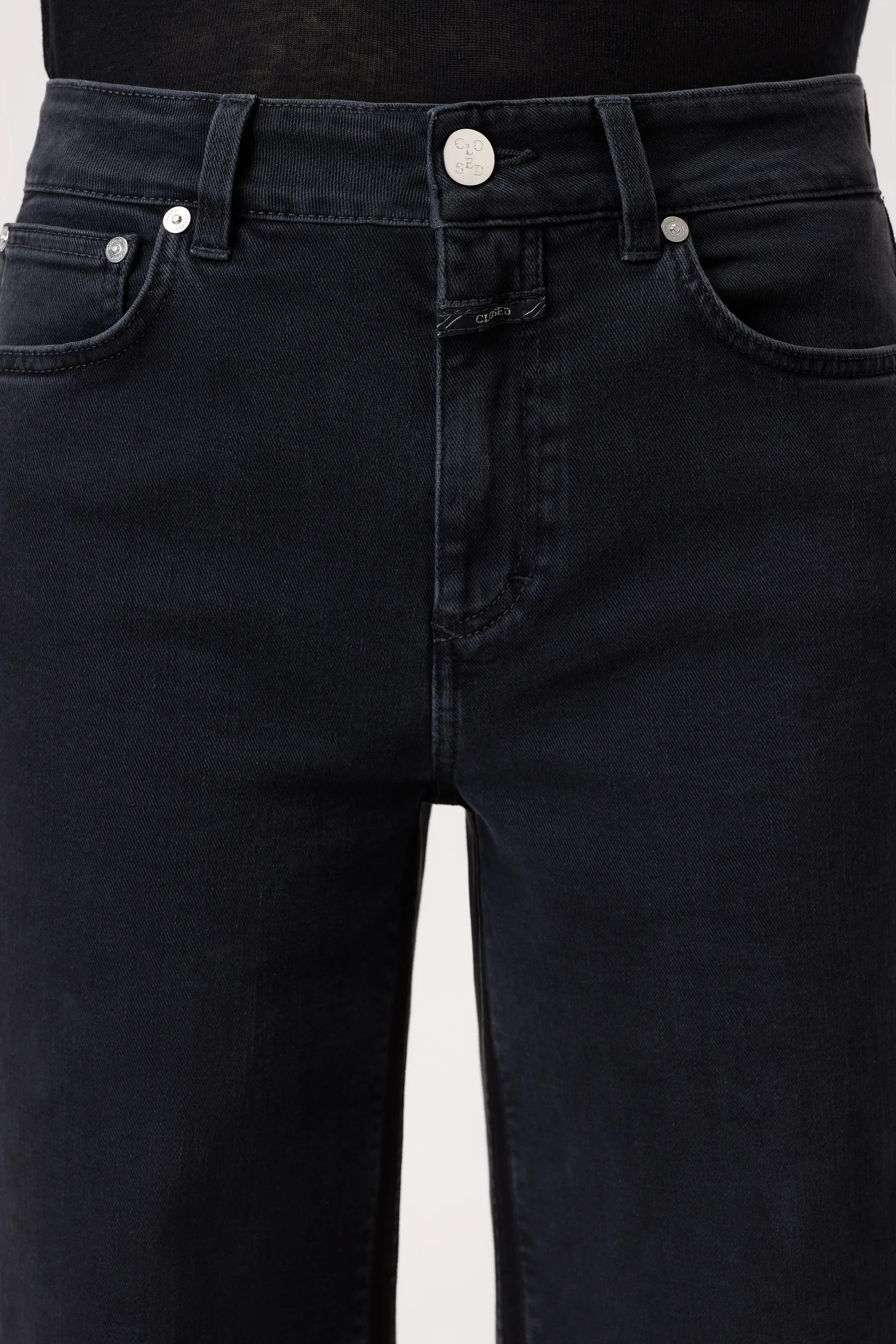 Close-up of a person wearing the CLOSED Glow Up high waist black denim jeans with button and zipper closure, belt loops, and front pockets. These jeans feature a classic five-pocket design and a straight-leg silhouette.