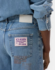 Someone wears light blue CLOSED Nikka Denim jeans and a matching shirt, highlighting the back pocket’s purple patch reading “CLOSED PRODUTTORE DI JEANS DAL 1978,” with a white label on the waistband.