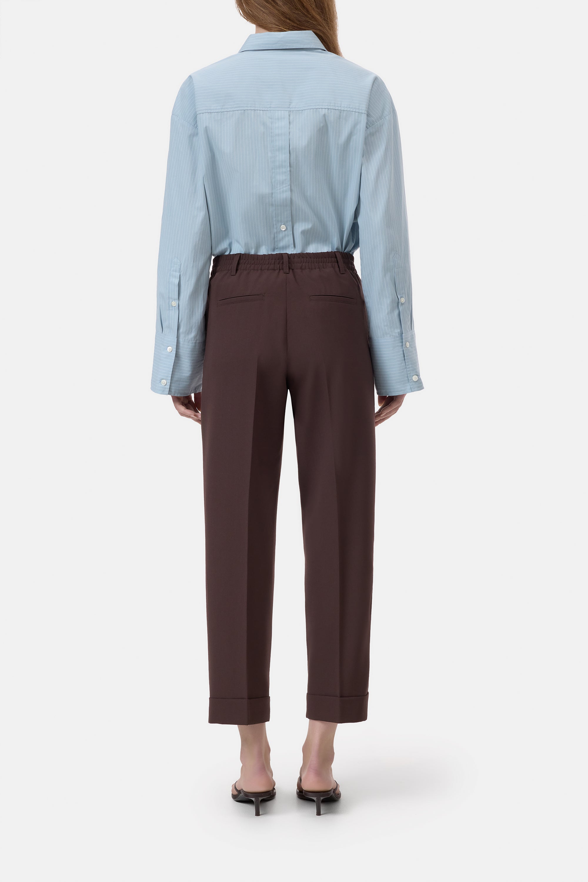 Souki light blue button-up shirt and cropped wool trousers by CLOSED, styled with black heels, back view.