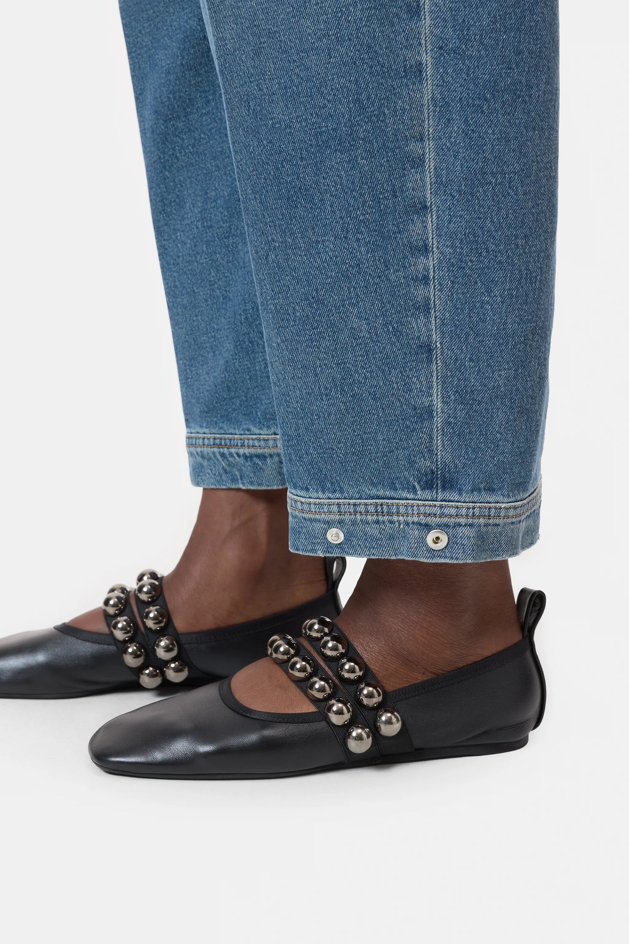 A person wearing CLOSED Rhannon Denim barrel-fit jeans in a vintage wash, paired with black flat shoes featuring two straps adorned with large silver beads.