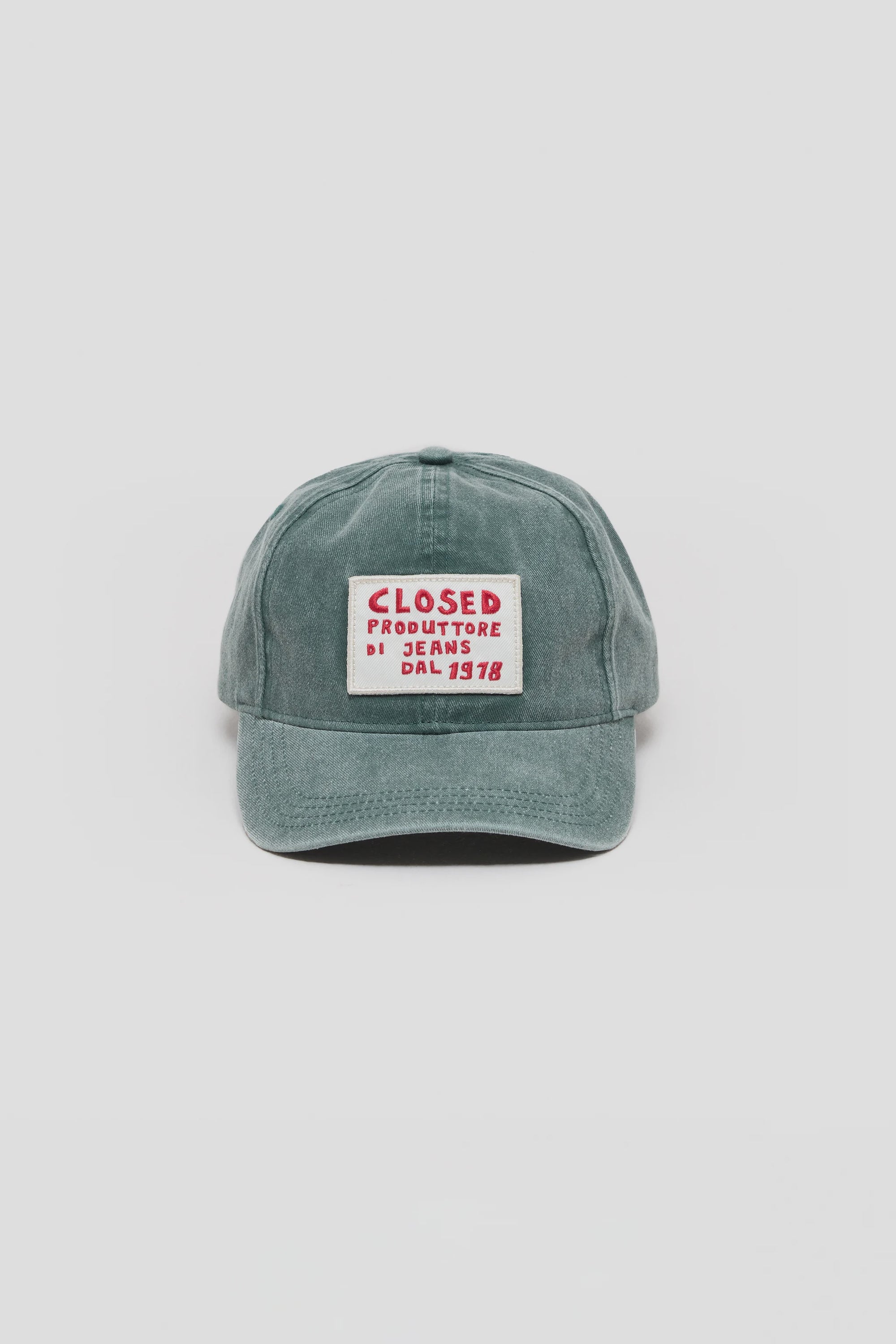 The CLOSED Cap is a green cotton hat with a washed finish, featuring a rectangular white patch on the front with red "CLOSED PRODUTTORE DI JEANS DAL 1978" text, an adjustable strap, and shown against a plain light background.