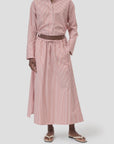 A person stands against a plain light background wearing a red and white vertically striped button-up shirt, the CLOSED Gathered Skirt with elasticated waistband (100% cotton), and white sandals.