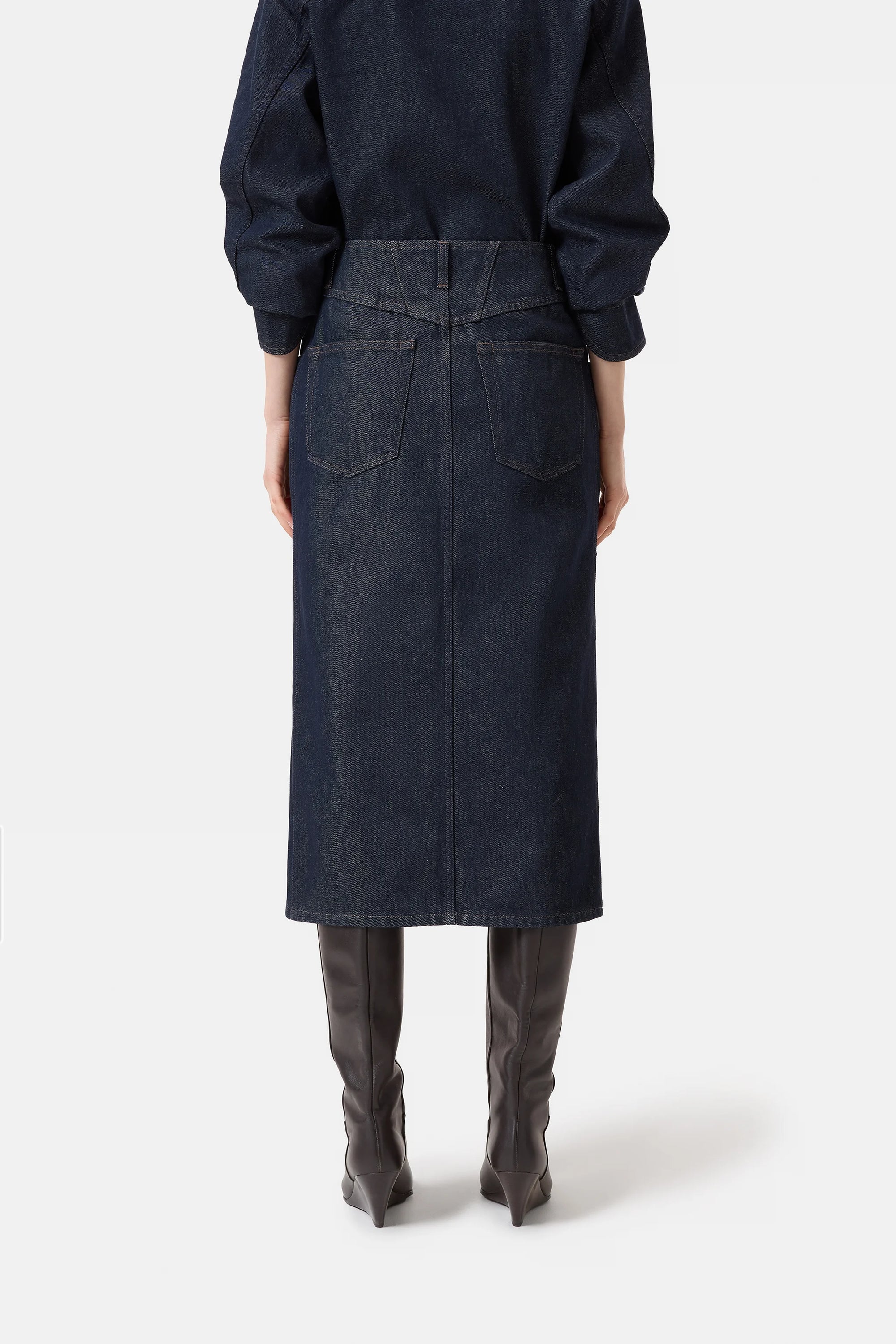 A person faces away in a CLOSED Zip Skirt—dark Italian Stay-Blue denim with back pockets and seam details—paired with a matching top and gray pointed-toe boots, all showcased against a plain white background.