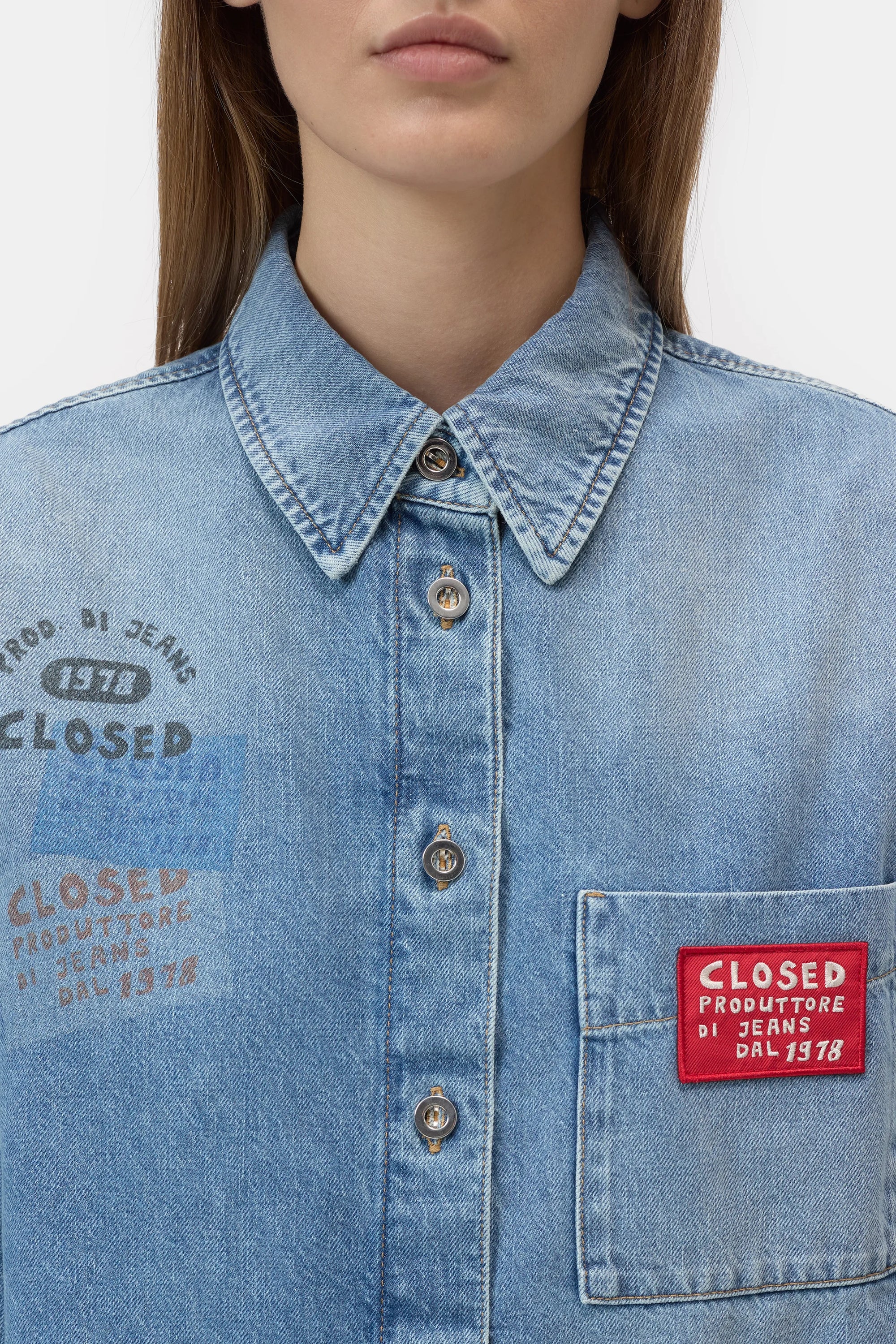 A woman wears the CLOSED Oversized Shirt featuring metallic buttons, a pointed collar, a red "CLOSED PRODUTTORE DI JEANS DAL 1978" patch, partial text above the pocket, and Italian craftsmanship.