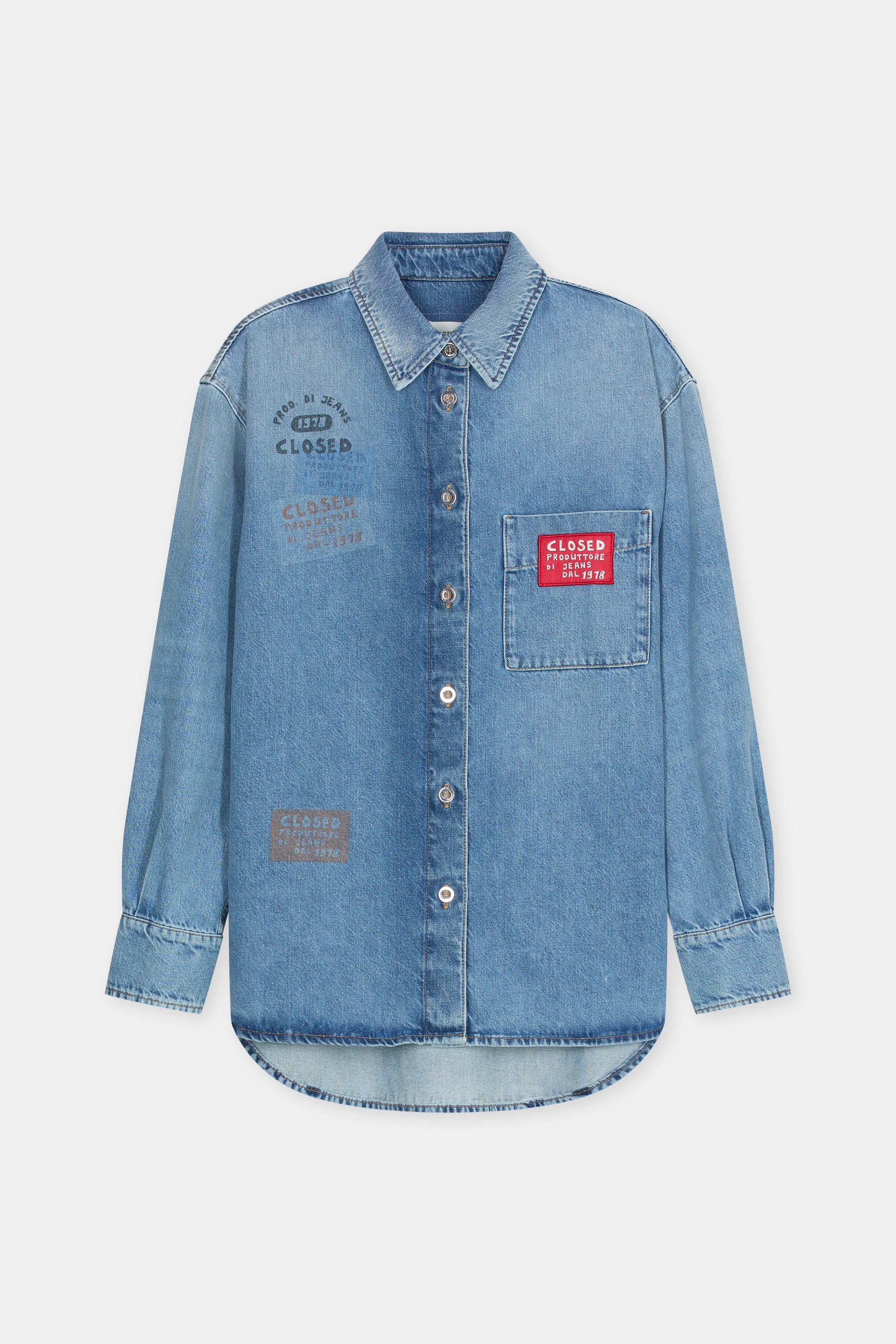The CLOSED Oversized Shirt is a light blue denim piece featuring a pointed collar, front pocket, and multicolored printed and embroidered patches with text designs on the chest and pocket areas.