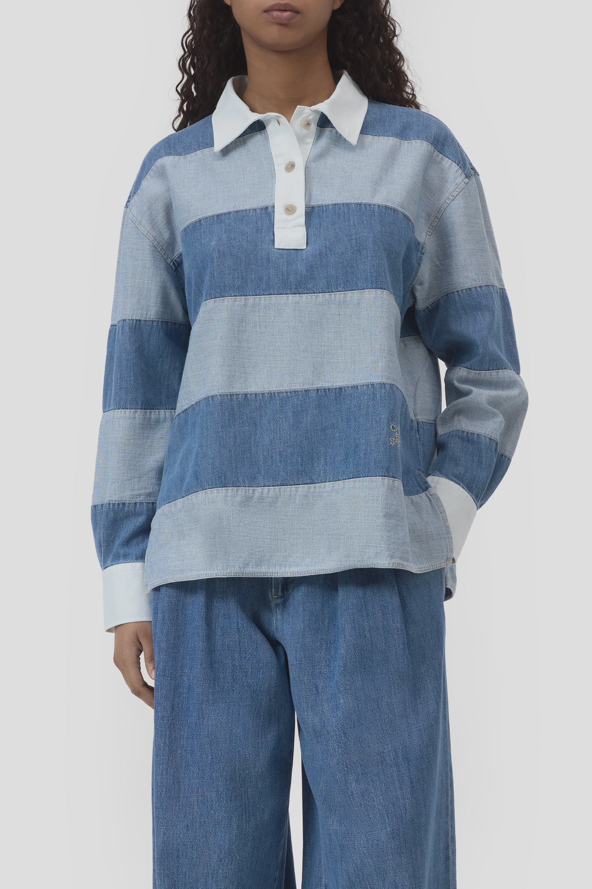 A person wears the CLOSED Rugby Shirt—long-sleeved, organic cotton with wide light and medium blue stripes, white collar and cuffs—paired with blue denim pants, standing against a plain background.