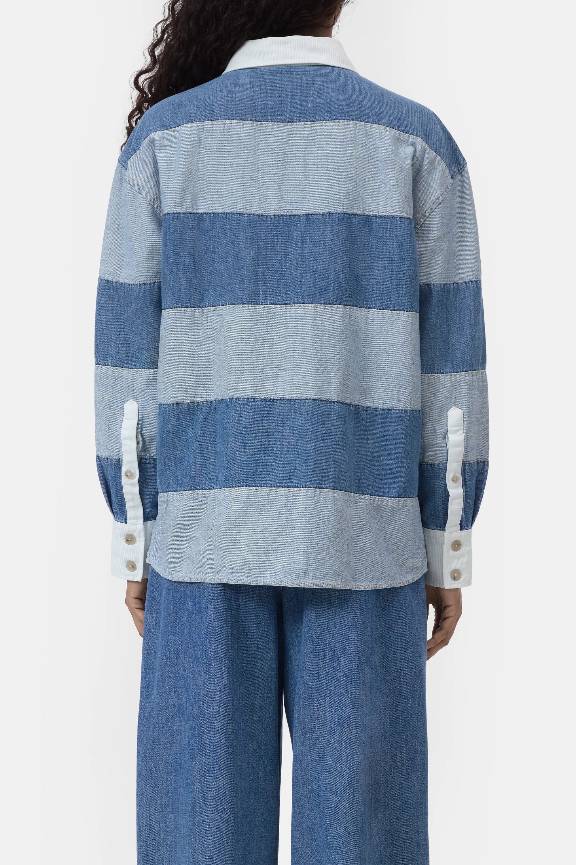 A person shown from the back wears a CLOSED Rugby Shirt in blue and light blue stripes with white cuffs and collar, paired with wide-leg blue denim pants.