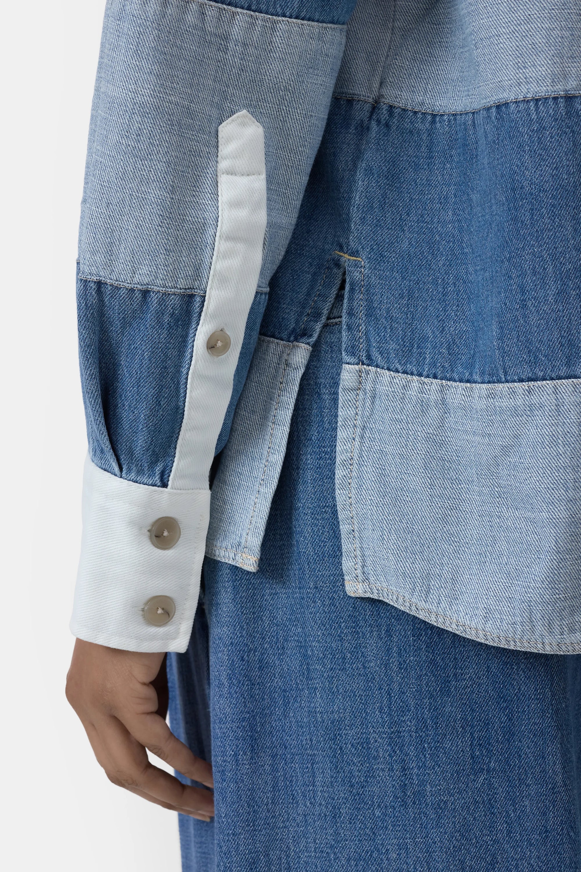 A close-up of a person wearing the CLOSED Rugby Shirt with color-blocked lightweight denim, white cuff with three buttons, and matching denim pants. Their hand is relaxed at their side.