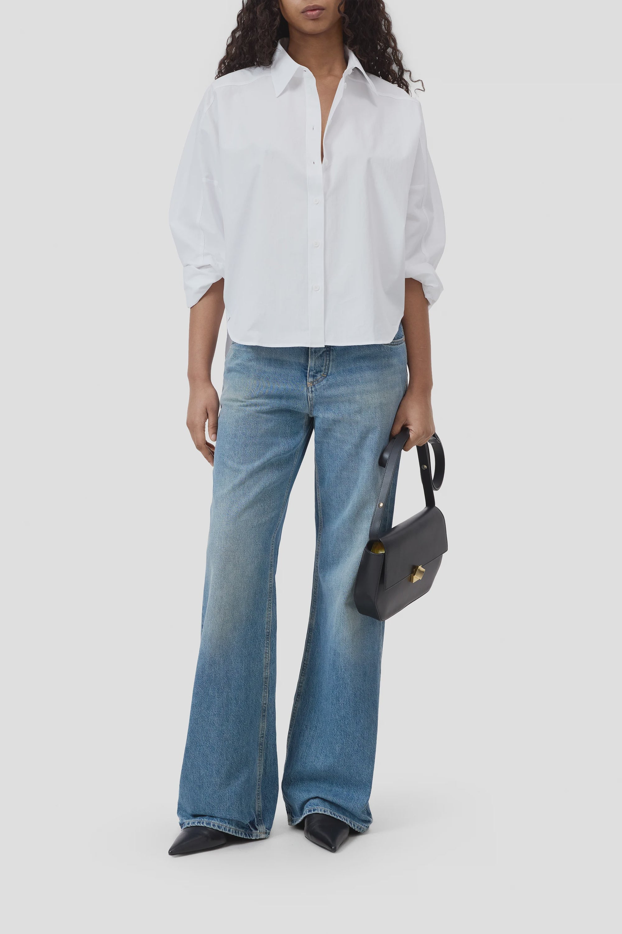 A person wears the CLOSED Gathered Shirt in white, blue wide-leg jeans, black pointed-toe shoes, and holds a black handbag against a plain background.