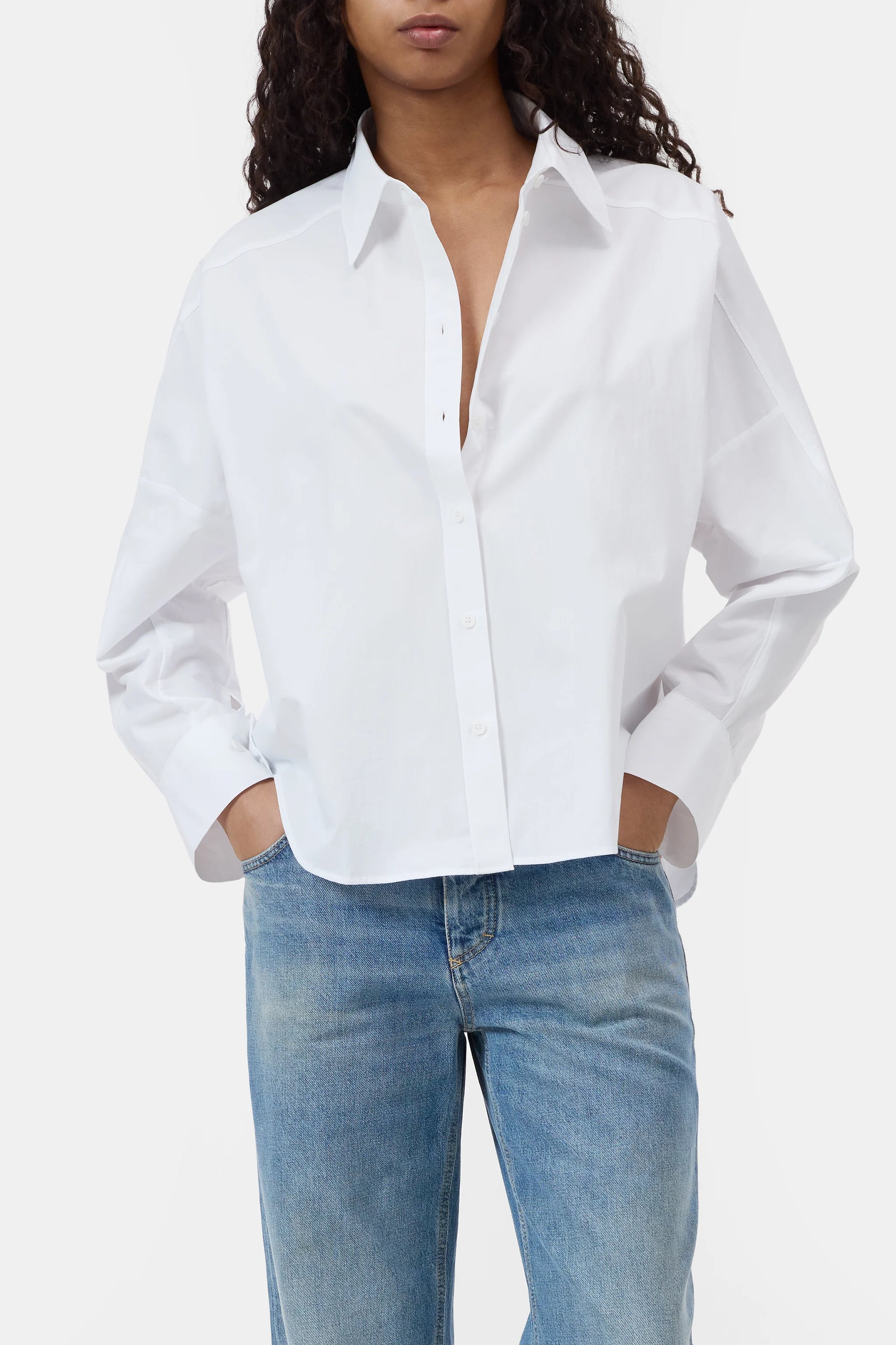 A person wearing the CLOSED Gathered Shirt, a relaxed-fit organic cotton blouse with sleeves rolled up, paired with light blue jeans and standing hands in pockets against a plain background.