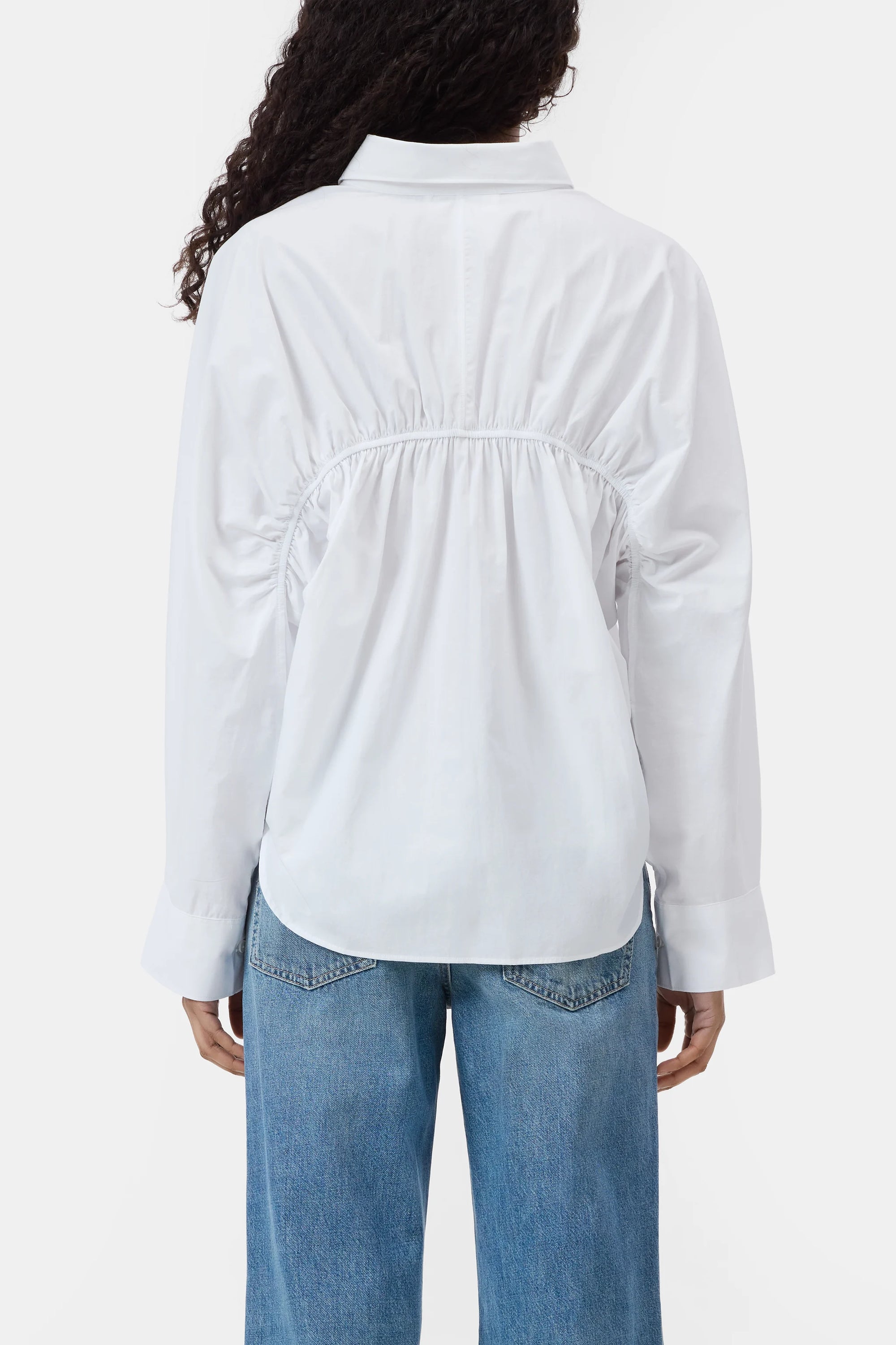 A person shown from behind wearing the CLOSED Gathered Shirt, a relaxed-fit white blouse with back gathers, paired with blue jeans.