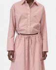 A person wears the CLOSED Gathered Shirt, a relaxed-fit women's blouse in pink and white vertical stripes with wide cuffs, paired with a matching high-waisted drawstring skirt. The coordinated set has a laid-back vibe, showing only the torso and upper legs.