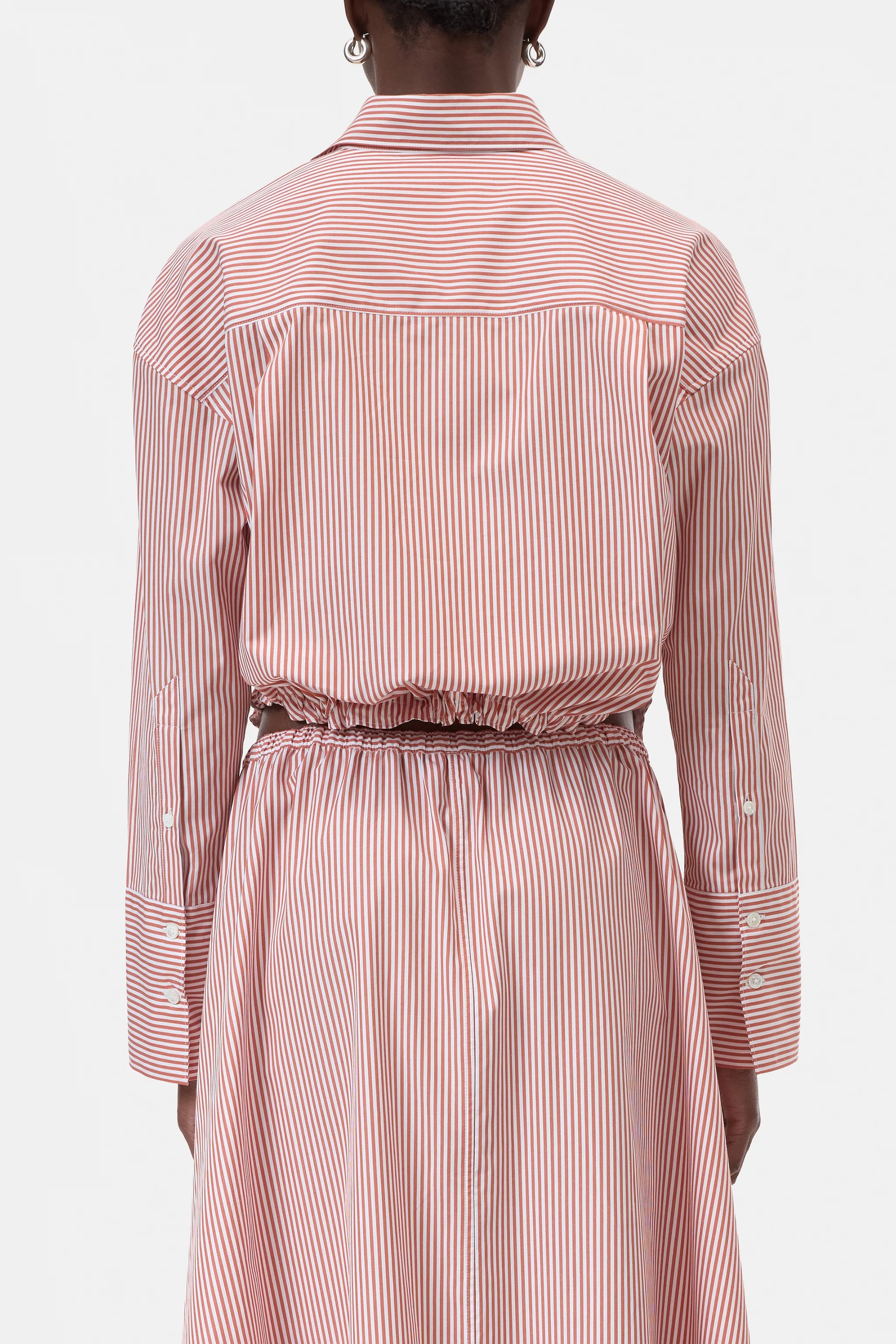 A person is shown from the back wearing the CLOSED Gathered Shirt, a women’s blouse dress with red and white vertical stripes, a cinched waist with gathered detail, buttoned sleeve cuffs, and a relaxed-fit silhouette.