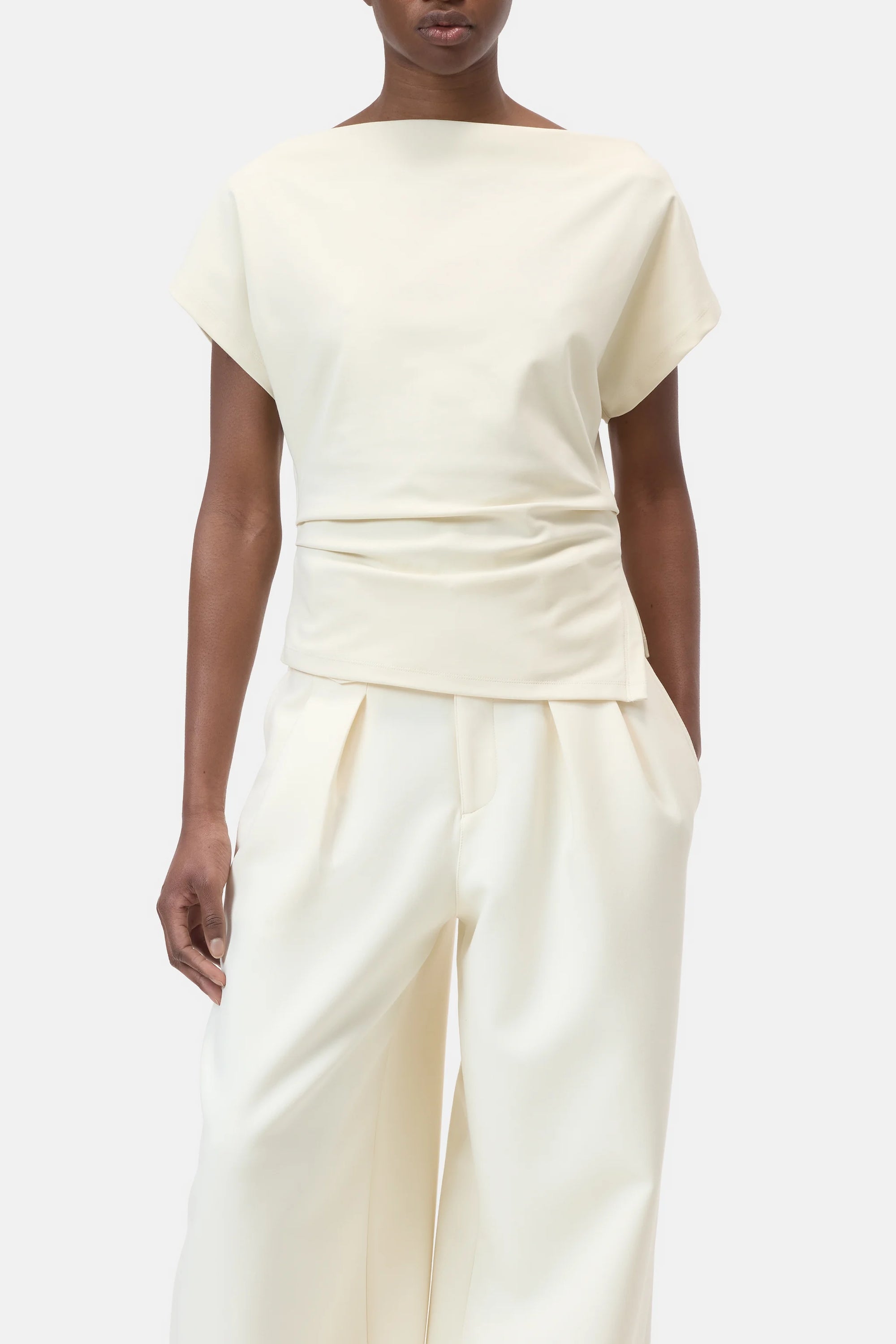 A person wears the CLOSED Off Shoulder Top in slim fit off-white cotton-elastane with a draped waist, paired with matching high-waisted wide-leg trousers, standing against a plain light background.